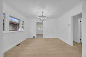Unfurnished dining area with light wood finished floors, a chandelier, a textured ceiling, and crown molding
