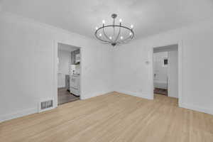 Unfurnished dining area featuring hanging lights, crown molding, light wood finished floors, and a textured ceiling