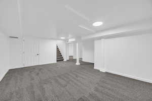 Finished below grade area featuring stairway and dark colored carpet