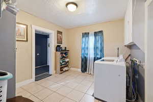 Laundry room featuring washer / clothes dryer, a textured ceiling, and light tile patterned floors