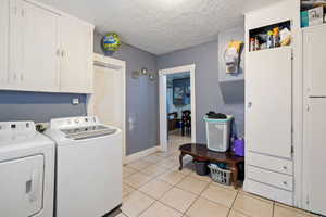 Laundry room with a textured ceiling, separate washer and dryer, light tile patterned flooring, and cabinet space