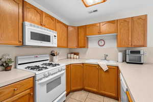 Kitchen featuring white appliances, light countertops, light tile patterned flooring, and wood finish cabinetry