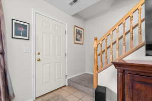 Foyer entrance with light tile patterned flooring and light carpet