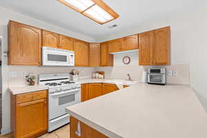 Kitchen with white appliances, light countertops, light tile patterned floors, a peninsula, and wood finish cabinets