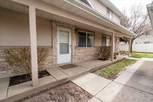 Doorway to property with brick siding, covered porch, and stucco siding