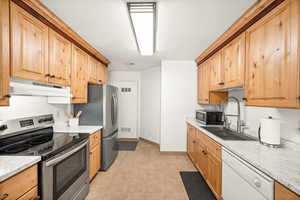 Kitchen with stainless steel appliances, light stone counters, and light wood finish cabinetry
