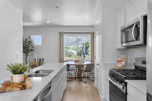 Kitchen with stainless steel appliances, white cabinets, light wood-style flooring, and a textured ceiling