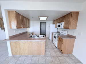 Kitchen with white appliances, a peninsula, a textured ceiling, wood finish cabinets, and light countertops
