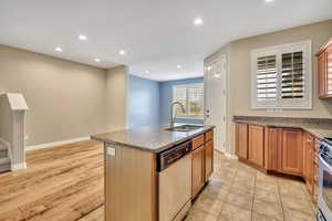 Kitchen with dark stone counters, stainless steel appliances, a kitchen island with sink, recessed lighting, and light wood finished floors
