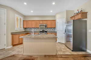 Kitchen with stainless steel appliances, light stone countertops, a center island with sink, wood finish cabinetry, and recessed lighting