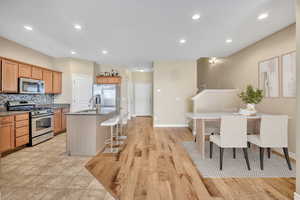 Kitchen with stainless steel appliances, a kitchen bar, light wood-style floors, decorative backsplash, and dark stone counters