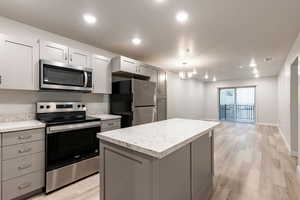 Kitchen with stainless steel appliances, light wood-type flooring, gray cabinetry, a center island, and a textured ceiling
