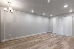 Empty room with light wood-style floors, a textured ceiling, hanging lights, and a smoke detector