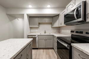 Kitchen featuring stainless steel appliances, gray cabinets, light wood-style flooring, a textured ceiling, and light stone counters