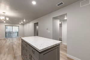 Kitchen with light wood finished floors, a kitchen island, gray cabinets, open floor plan, and a chandelier
