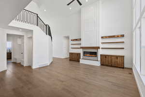Unfurnished living room with recessed lighting, a large fireplace, a high ceiling, a ceiling fan, and light wood finished floors