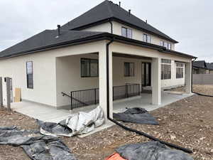 Rear view of house featuring a patio, stucco siding, and a shingled roof