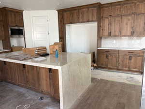 Kitchen with stainless steel microwave, a kitchen island, light stone counters, backsplash, and a textured ceiling