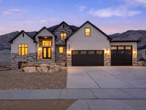 View of front of home with stucco siding, stone siding, driveway, an attached garage, and a mountain view