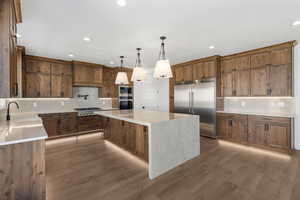 Kitchen with tasteful backsplash, a kitchen island, built in appliances, pendant lighting, and light stone counters
