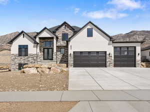 View of front facade with a mountain view, stone siding, stucco siding, and concrete driveway