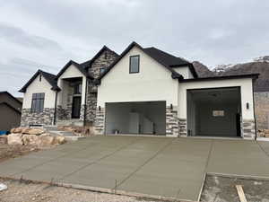 View of front facade featuring stone siding, stucco siding, driveway, and a garage