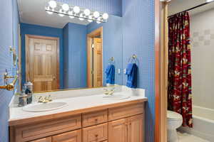 Full bathroom with wallpapered walls, double vanity, shower / bath combo, and light tile patterned floors