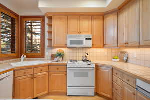 Kitchen with tile counters, white appliances, and backsplash