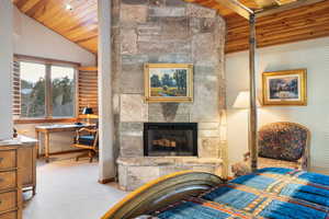 Bedroom with wallpapered walls, a stone fireplace, light carpet, wood ceiling, and a desk