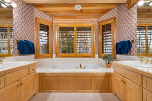 Full bathroom featuring wallpapered walls, two vanities, beam ceiling, and a garden tub
