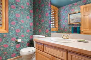 Half bathroom featuring wallpapered walls and vanity