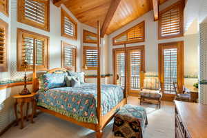 Bedroom featuring wallpapered walls, lofted ceiling with beams, light colored carpet, multiple windows, and wooden ceiling