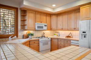 Kitchen with white appliances, open shelves, decorative backsplash, tile counters, and recessed lighting
