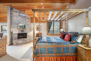 Carpeted bedroom featuring a tiled fireplace and wood ceiling