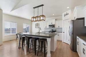 Kitchen with a kitchen breakfast bar, dark countertops, white cabinetry, stainless steel appliances, and a kitchen island with sink