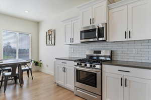 Kitchen with stainless steel appliances, white cabinets, decorative backsplash, light wood finished floors, and recessed lighting