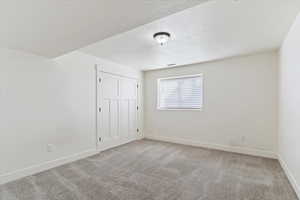 Unfurnished bedroom with light carpet, a closet, and a textured ceiling