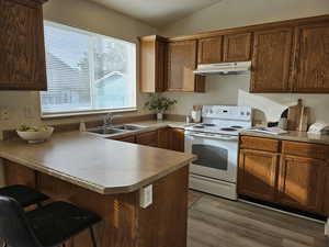 Kitchen with white electric stove, a peninsula, a kitchen breakfast bar, vaulted ceiling, and dark wood-type flooring