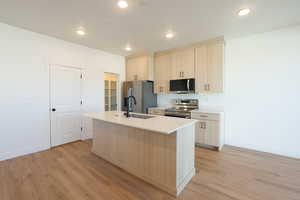Kitchen with an island with sink, stainless steel appliances, light wood finish cabinetry, light wood finished floors, and recessed lighting