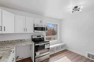 Kitchen with stainless steel appliances, light stone counters, white cabinets, and light wood-style floors