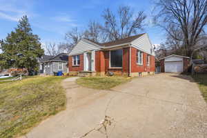 Bungalow-style home featuring an outbuilding, brick siding, a garage, concrete driveway, and a front yard