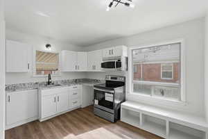 Kitchen with stainless steel appliances, light wood-type flooring, white cabinetry, light stone counters, and healthy amount of natural light