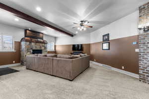 Living room featuring a stone fireplace, light colored carpet, ceiling fan, beamed ceiling, and recessed lighting