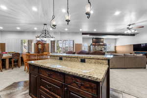 Kitchen featuring dark wood finish cabinetry, open floor plan, light colored carpet, and light stone counters