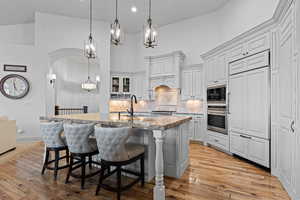 Kitchen with a breakfast bar area, an island with sink, built in appliances, light wood-style flooring, and backsplash