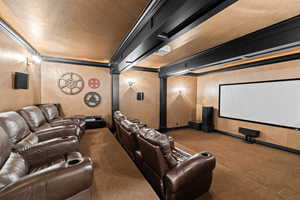 Carpeted cinema room featuring a textured ceiling, crown molding, and decorative columns