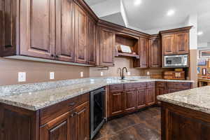Kitchen with beverage cooler, dark wood finish cabinets, stainless steel microwave, light stone counters, and open shelves