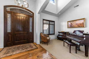 Foyer with vaulted ceiling, hanging lights, light wood-style flooring, light carpet, and arched walkways