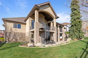 Back of property featuring a balcony, stucco siding, a patio area, and a yard