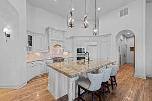Kitchen with arched walkways, a breakfast bar, white cabinets, light stone counters, and a high ceiling